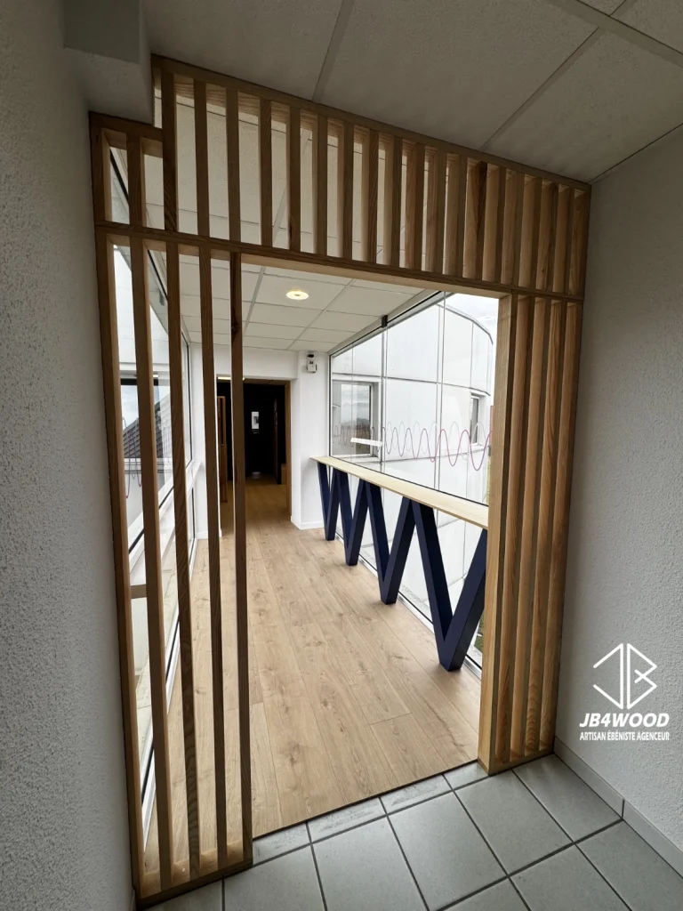 Conception, fabrication et installation d'un claustra bois en frêne massif pour une séparation de salle de pause d'une entreprise, on apperçoit en arrière plan le mange debout avec piètement "en V" réalisé également par JB4WOOD.